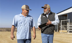 Dairy Farmers of America employee holding a tablet and walking next to a farmer