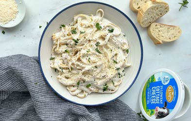 Bowl of cottage cheese on a table next to grated Parmesan cheese, cottage cheese and three slices of bread.