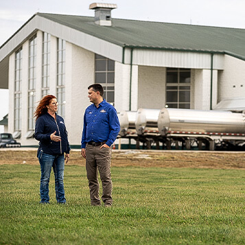 A farmer and operator have a discussion while standing in a field of grass.
