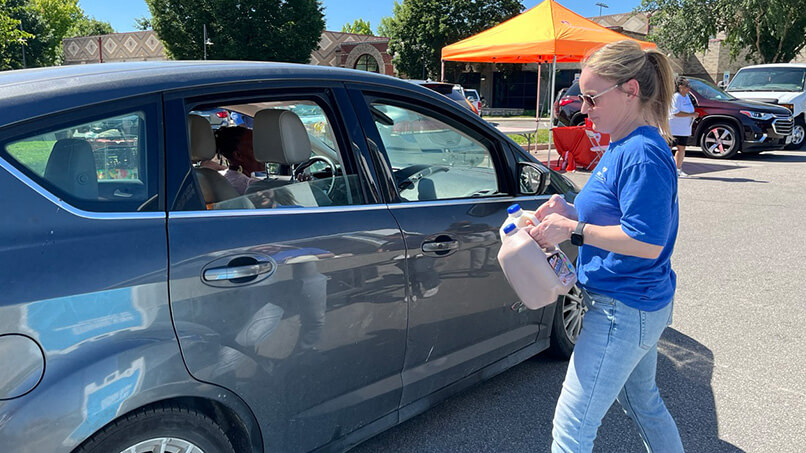 A volunteer with DFA Cares Foundation prepares two gallon jugs of milk for a car.