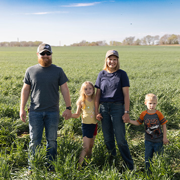 Farmers pose with their children in a field of grass.